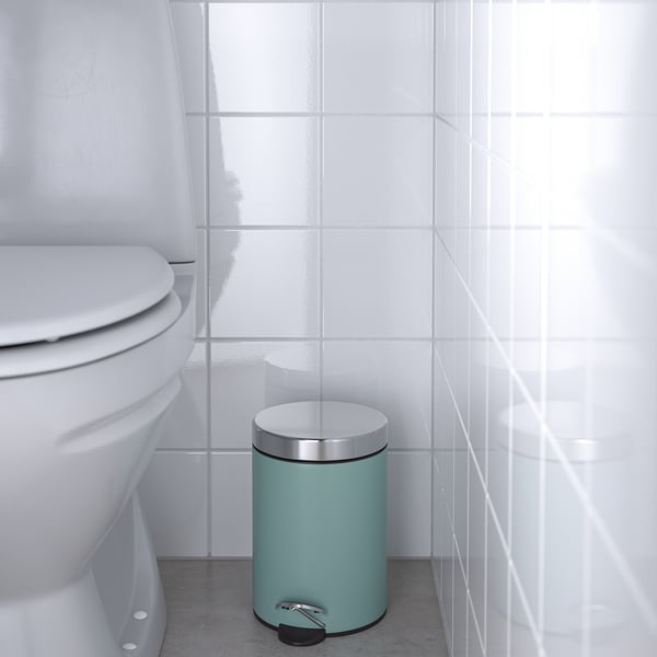 Pequeño cubo de basura verde en el baño con azulejos blancos cerca del inodoro con pedal para uso manos libres.