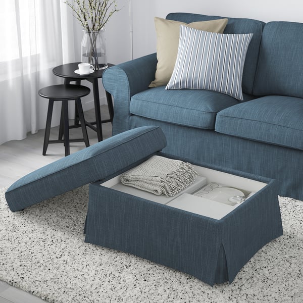 Sofá azul con reposapiés oculto. Almohadas, taza y manta a la vista.