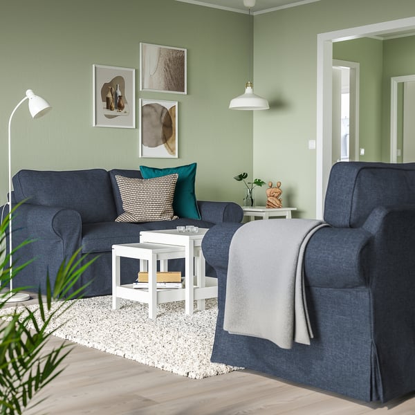 Luminosa sala de estar con sofá y sillón azul EKTORP, mesa de centro blanca, paredes verdes. El sofá y el sillón tienen cojines gruesos y reversibles.