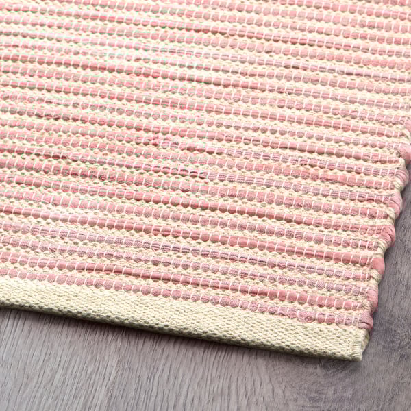 Alfombra tejida a mano en rosa pastel y beige, que demuestra una artesanía de alta calidad y un diseño único.