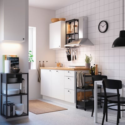 Moderna configuración de cocina blanca con encimera, fregadero y unidades de almacenamiento. Incluye armario de pared y estante para colgar utensilios.