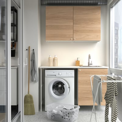 Una configuración de lavandería compacta con gabinetes ENHET en electrodomésticos blancos estilo madera y una toalla a rayas.