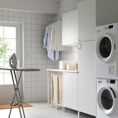 Moderna configuración de lavandería con gabinetes ENHET blancos, lavadora / secadora apilada, ropa, tabla de planchar y almacenamiento.