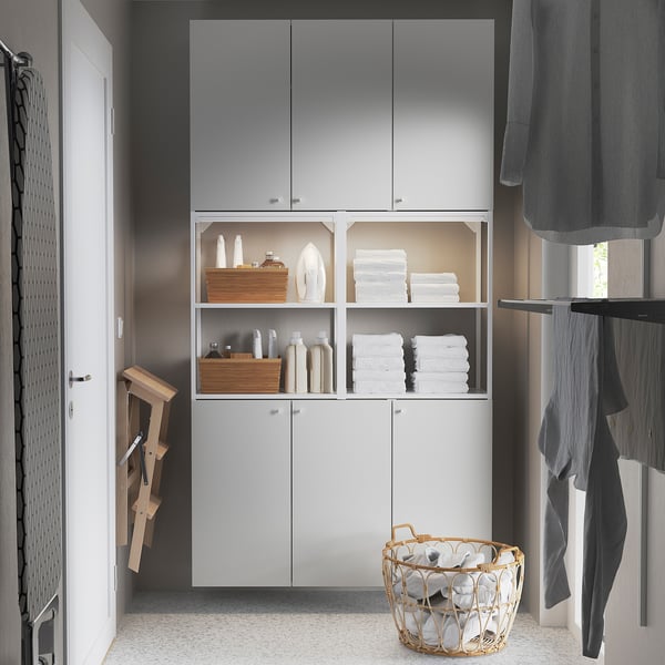Armario ENHET blanco con estantes, puertas y toallas abiertos. Cortina gris, percha de madera.