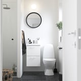 Moderno baño blanco con mueble flotante, espejo redondo y elegante inodoro. Diseño limpio y minimalista.