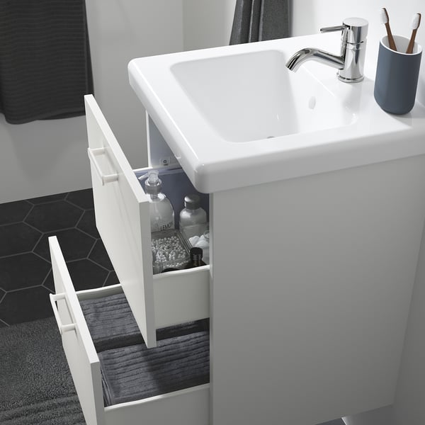 Moderno mueble con lavabo de baño con cajones, artículos de tocador y una alfombra gris debajo.