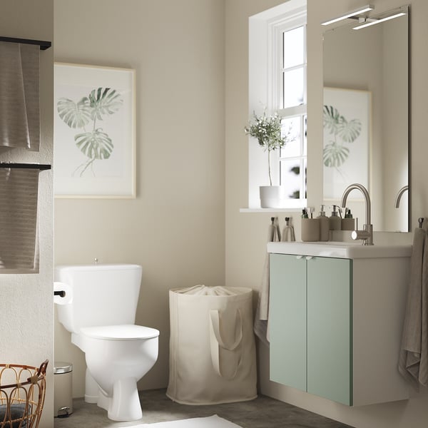 Baño sereno con gabinete ENHET verde, inodoro blanco y decoración tropical.