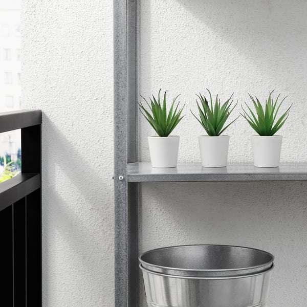 Tres plantas artificiales en macetas blancas se alinean en un estante, no requieren cuidados y son adecuadas para uso en interiores o exteriores.