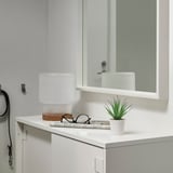 Baño moderno con encimera blanca, pequeño lavabo de cerámica blanca, espejo de seguridad y diminuta planta verde artificial FEJKA.