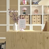 Marco de fotos rosa de doble cara, FIKONTRÄD, sobre escritorio de madera, rodeado de estanterías con libros y decoración, destacando su pequeño tamaño.