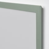 Un primer plano de un marco de fotos verde con cubierta de plástico transparente, apoyado contra una pared lisa.