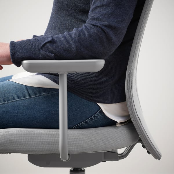 Silla ergonómica con respaldo de malla, reposabrazos, persona con camisa oscura y jeans.