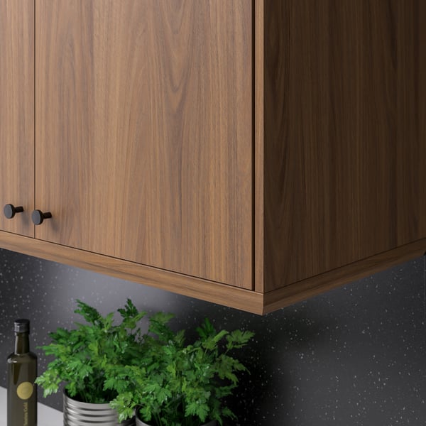 Mueble de cocina de madera con pomos oscuros y salpicadero gris. Hierbas y botella en el mostrador.