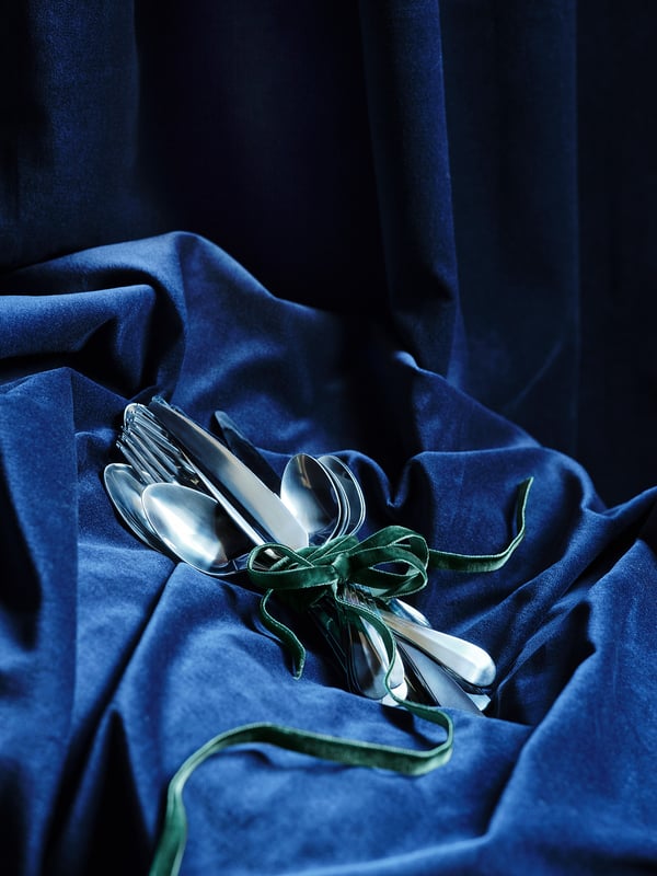 Cubiertos GAMMAN plateados atados con cinta verde sobre tela azul.