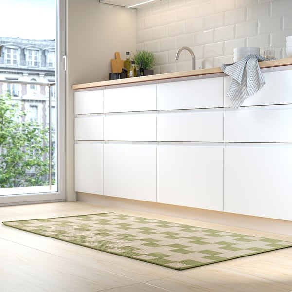 Cocina moderna con armarios blancos, suelo de madera clara y estera GÅNGSTIG verde.