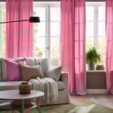 Las cortinas rosas enmarcan grandes ventanas, agregando color y privacidad. El sillón neutro con almohadas completa un espacio acogedor y acogedor.