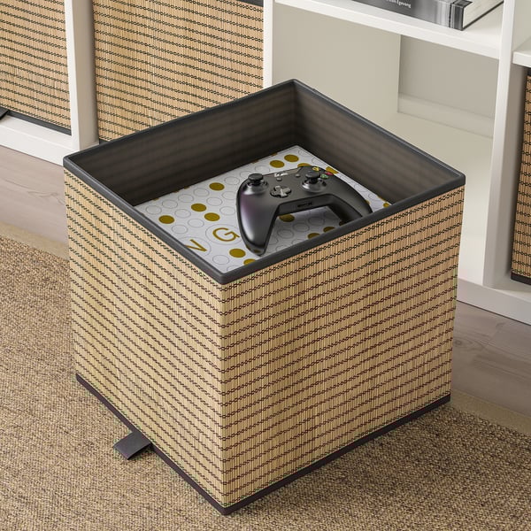 Una caja estampada en negro y beige con un asa, que contiene un controlador de juegos, ideal para organizar los estantes kallax.