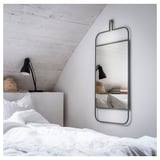 Un dormitorio moderno con un espejo GRANVÅG de pared en color verde. El espejo tiene forma rectangular con un estante para accesorios.