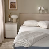 Cama pulcra con edredón GRÄSROTSFLY, lyocell sedoso, cabecero beige. Al lado del cajón hay una lámpara, un jarrón con plantas secas. Decoración minimalista.