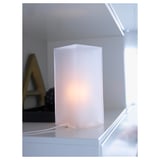 Una lámpara de mesa de vidrio esmerilado blanco, que emite una suave luz ambiental, sentada sobre una superficie.