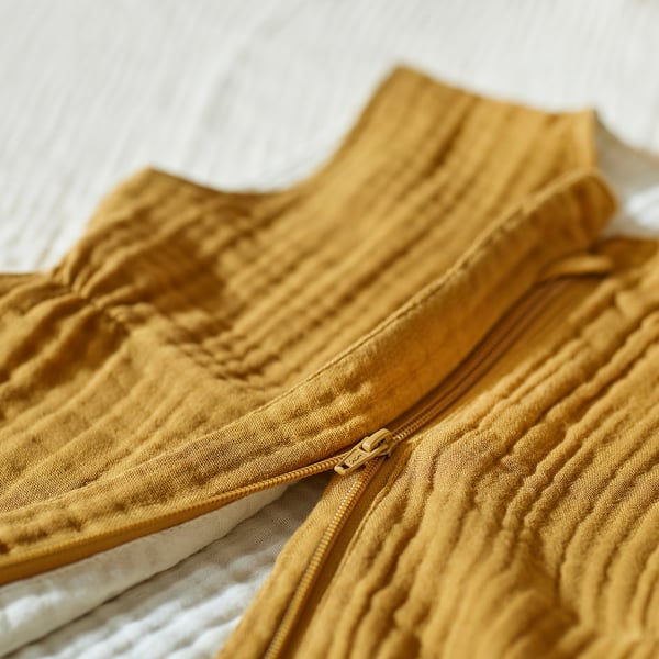 Primer plano de un saco de dormir de color mostaza con una cremallera visible en todo su cuerpo, que muestra su tejido suave y texturizado.