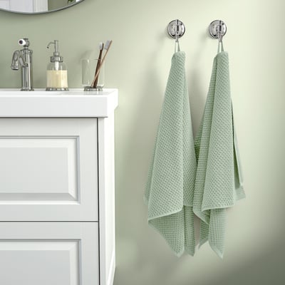 Las toallas verdes cuelgan cerca del fregadero blanco con dispensador de jabón.