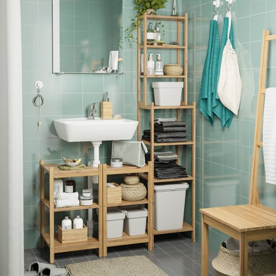 Baño con azulejos verdes, lavabo blanco, estantes de madera y toallas azules. Incluye papeleras HÅLLBAR para el almacenamiento, algunas con tapa blanca.
