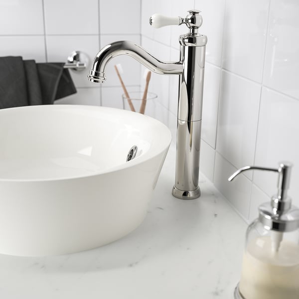 Grifo moderno cromado, manijas de cerámica, encima de un gran lavabo blanco con dispensador de jabón.