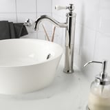 Grifo moderno cromado, manijas de cerámica, encima de un gran lavabo blanco con dispensador de jabón.