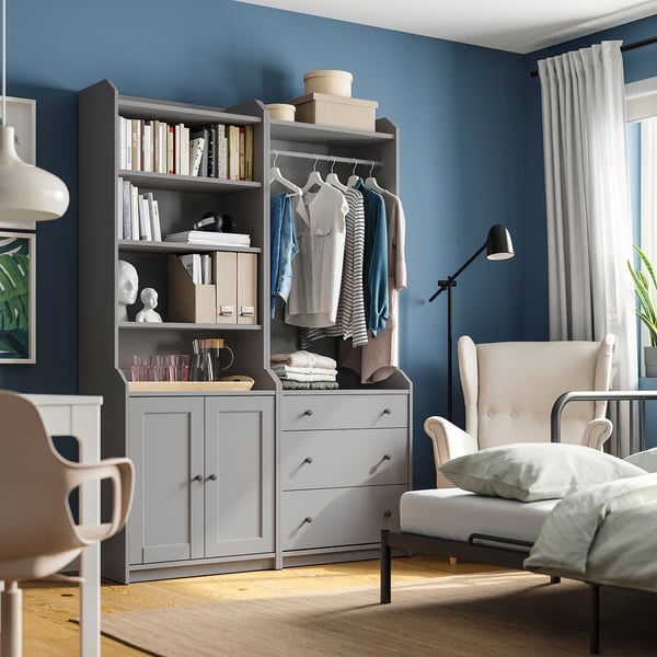 Dormitorio moderno con almacenamiento HAUGA gris, ropa, libros y decoración. Paredes azules, suelo de madera.