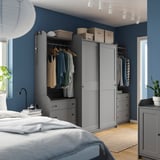 Dormitorio moderno azul con armarios HAUGA grises, perchas y ropa de cama blanca.