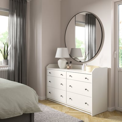 Dormitorio con tocador HAUGA blanco, espejo redondo, lámparas y paredes rosas.