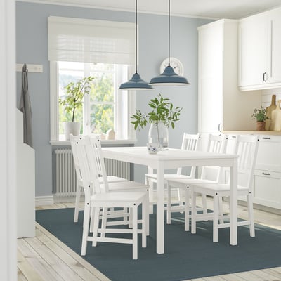 Cocina moderna con mesa HAUGA blanca, seis sillas a juego, alfombra azul, luces colgantes y plantas.