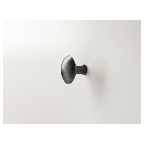 Gancho simple montado en la pared, acabado oscuro. Se fija verticalmente sobre una superficie lisa y ligera. Diseño duradero y minimalista.