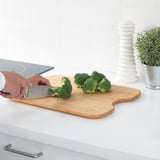 Persona cortando brócoli en la tabla de cortar de bambú HÖGSMA en la encimera de la cocina. La tabla tiene un agarre antideslizante.