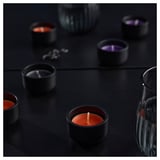 Cuatro candelitas encendidas sobre superficie oscura, que emiten una luz cálida y un aroma suave.