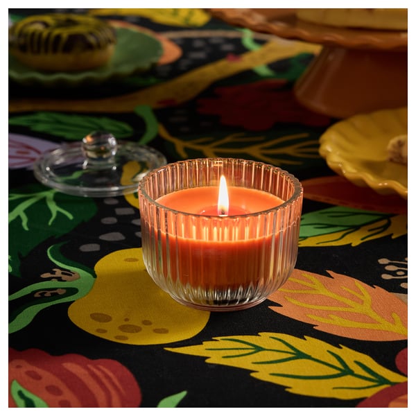 Una vela HÖSTAGILLE encendida en un frasco estriado con tapa, que emite un aroma a sándalo, pachulí y abeto.