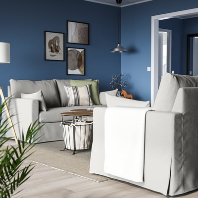 Acogedora sala de estar azul con sofá gris HYLTARP, mesa de centro blanca, luz colgante, arte y plantas.