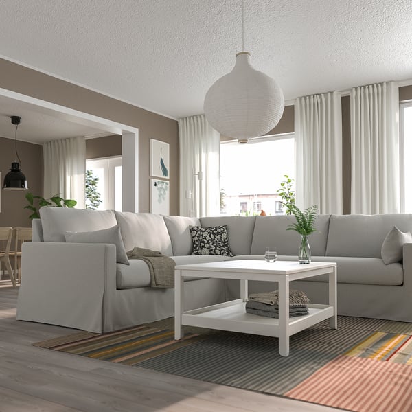 Sofá seccional en forma de L en una habitación luminosa con alfombra, mesa de centro y ventanas.