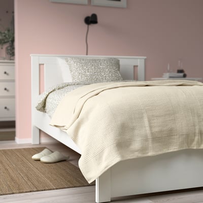 Acogedor dormitorio con colcha INDIRA sobre cama doble, algodón blanquecino, paredes rosas, suelo de madera.