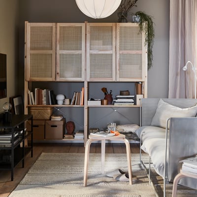 Sala de estar con estantería IVAR, puertas de madera clara, libros, decoración y una pequeña mesa, iluminada por una lámpara colgante.