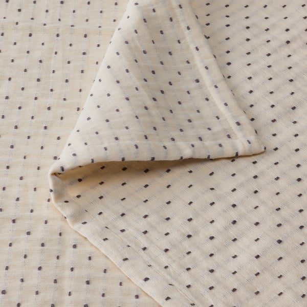Colcha blanca rota con costuras en gris oscuro, textura suave de algodón.