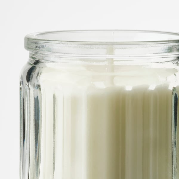 Vela de frasco de vidrio transparente con crestas verticales, rellena de cera blanquecina, vista superior.