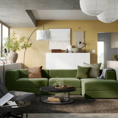 Sala de estar moderna con un gran sofá JÄTTEBO verde, alfombra tejida y una gran planta.