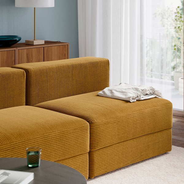 Sofá modular mostaza con tumbona, lámpara, cuenco y ventana.