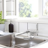 Fregadero de cocina moderno con grifería JUTTERN cromada y dispensador negro. Estilo limpio y minimalista con armarios blancos.