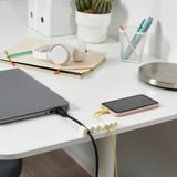 La imagen muestra un escritorio con una computadora portátil, un teléfono inteligente cargando y organizadores de cables KALKSTUFF que mantienen los cables ordenados.