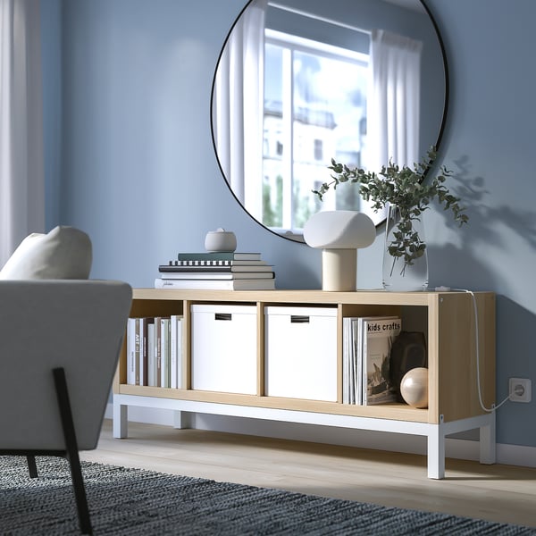 Unidad de almacenamiento KALLAX con libros, jarrones y revistas junto a la silla y la ventana.