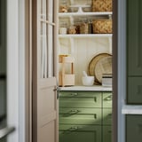 Estante de cocina con cesta verde KANELMOTT que contiene frutas y patatas, diseño de ratán hecho a mano.