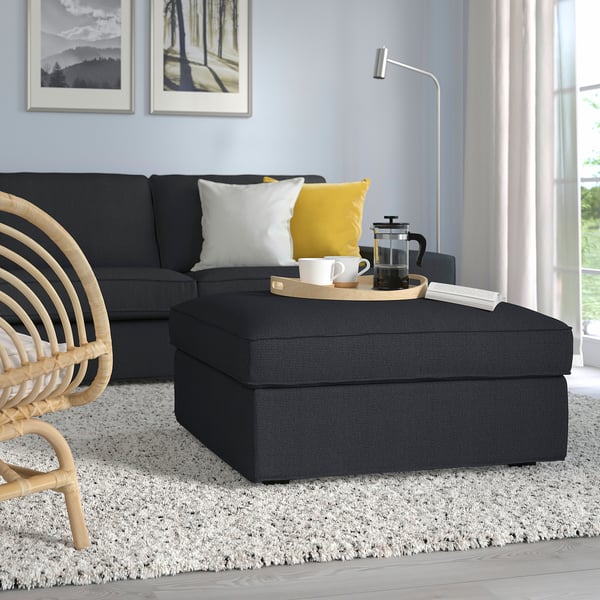 Gran reposapiés KIVIK gris con almacenaje, tapicería de tela, delante de sofá negro.
